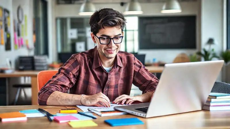 Estudiante en oficina moderna con notas y laptop